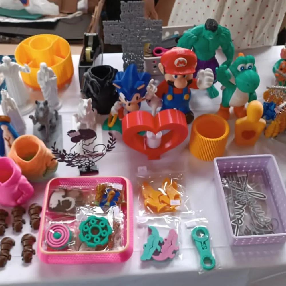 Mesa com várias peças impressas em 3D pela Dom Blue 3D: bonecos, cruzes, porta-objetos, chaveiros e miniaturas coloridas